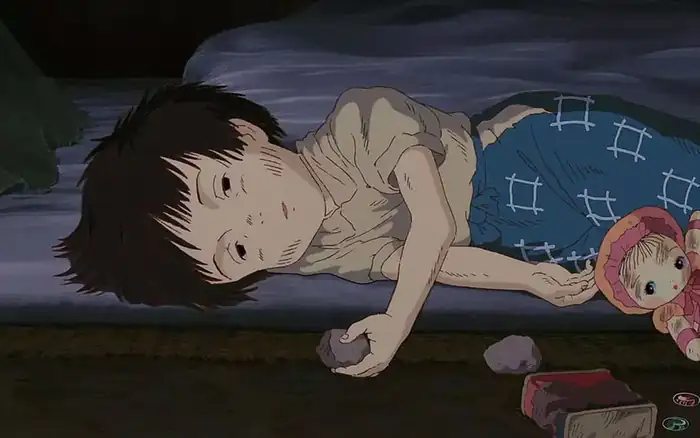 《螢火蟲之墓》中瘦弱少年疲憊橫臥，手握石頭，身旁有舊玩偶，神情哀戚