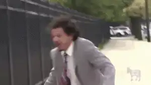 穿著灰色西裝的男子手持麥克風狂奔至鐵欄杆前，單手攀著欄杆仰天嘶吼，接著在強風吹亂頭髮下持續對著麥克風崩潰尖叫。出自《埃里克・安德烈秀》。